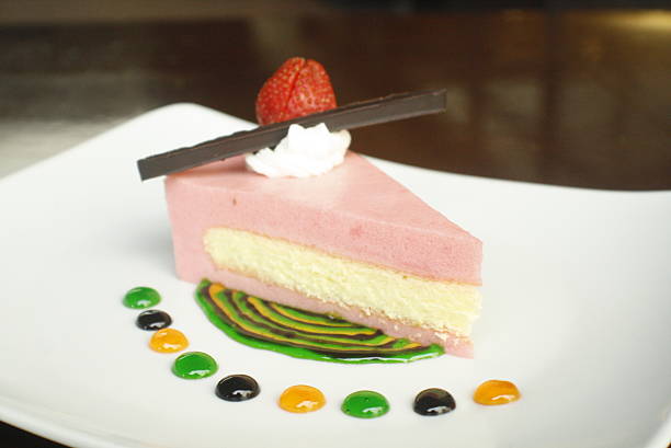 Elegant slice of strawberry mousse cake, garnished with a fresh strawberry and chocolate Presented on a white plate with colorful sauce artistry