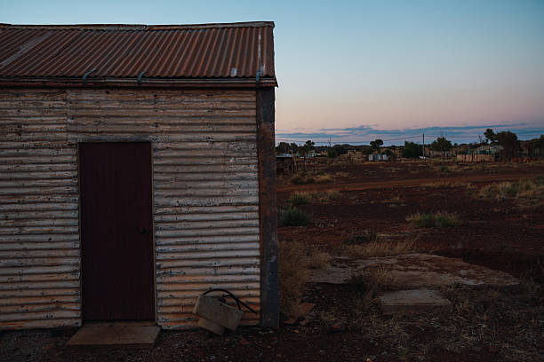Corrugated iron shack standing in a dusty outback landscape during twilight, showing solitude
