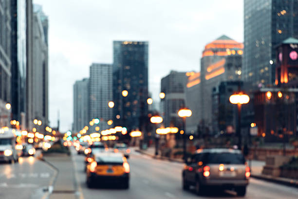 Evening traffic moves steadily along a downtown Chicago street as skyscrapers rise on both sides. Blurred headlights and taillights reflect the rhythm of urban life, capturing the energy of a busy American city during rush hour.