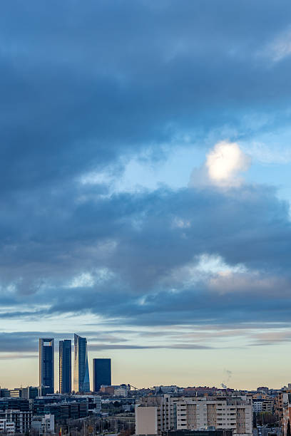 Madrid. Spain. Madrid cityscape featuring modern skyscrapers of the cuatro torres business area rising above residential buildings and urban infrastructure under a dramatic sky at twilight