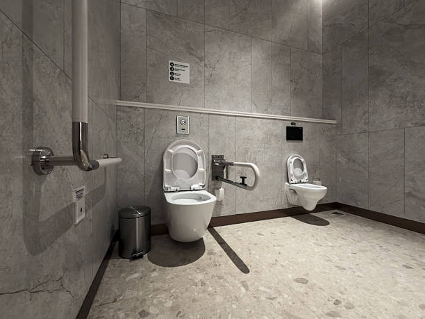 A sleek, industrial-style restroom featuring two white toilets against gray concrete walls and floors. The space is minimalistic, clean, and functional, ideal for commercial or public use.