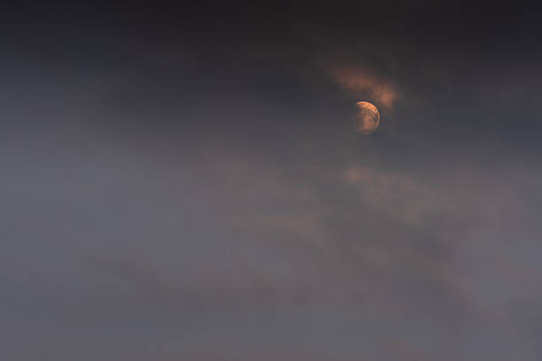 Moon partially hidden by heavy clouds in dark evening sky, minimalist celestial scene with moody atmosphere and soft natural light