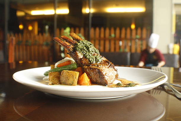 Exquisitely prepared rack of lamb, crusted with fresh herbs and served with roasted vegetables on a white plate This gourmet dish is presented in a dimly lit restaurant