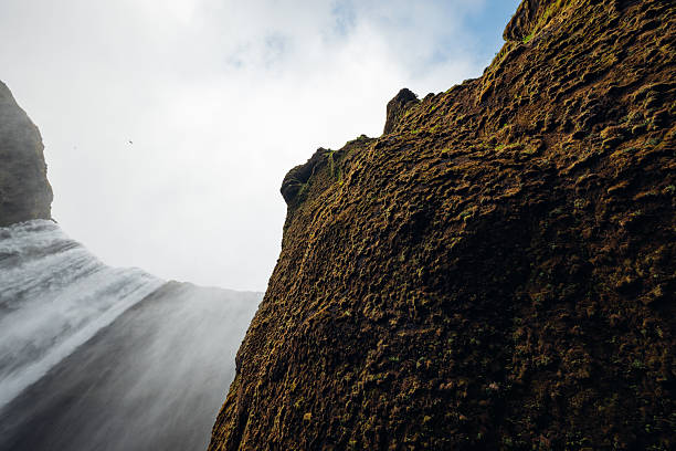 Skogafoss waterfall thunders down a moss-clad cliff, sending mist into a bright sky — dramatic, rugged Icelandic landscape showcasing raw water power and untouched wilderness