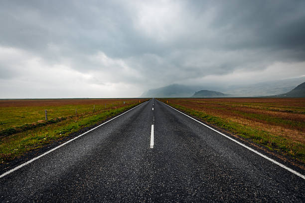 Asphalt road stretching into the distance through a vast, rugged landscape under a dramatic, cloudy sky, symbolizing travel, journey, and the open road in Iceland's unique nature