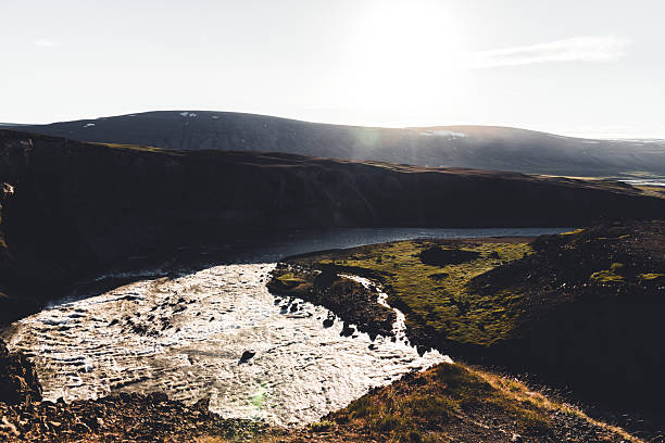 Iceland's Hvítá river flowing rapidly through a green and rocky canyon under a bright afternoon sunlight, highlighting the rugged natural beauty and powerful water