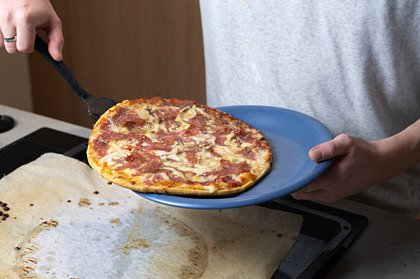 hands transferring pizza using spatula to parchmentlined tray, golden edges and bubbling cheese, handson meal prep, homemade comfort food moment