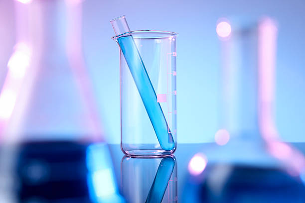 Different glassware with blue liquid on mirror surface against color background