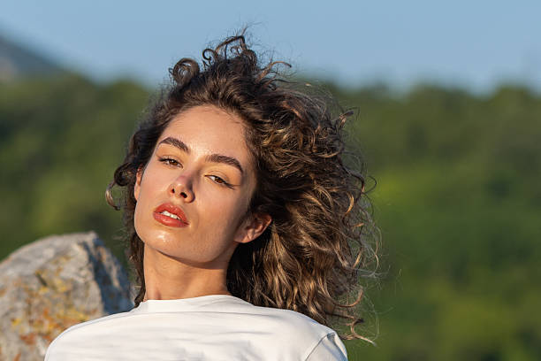 A pretty young woman's curly hair dances in the wind as she enjoys the outdoors.