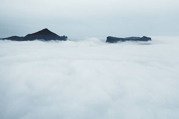 Icelandic mountains emerge from an expansive blanket of heavy low-lying fog and cloud cover, creating a dramatic, serene, and mystical mood in a remote, untouched natural landscape