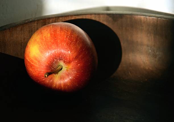 Red apple in sunlight in wooden bowl