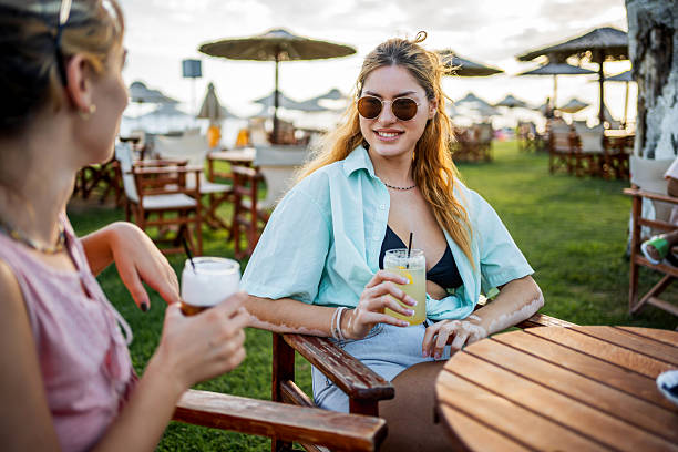 Young adult friends enjoying drinks and conversation at an outdoor beach bar restaurant during sunset