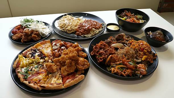 A diverse selection of delicious buffet items including spicy fried chicken cheesy pizza slices pasta with two sauces and traditional korean dishes like bulgogi are neatly arranged on a table