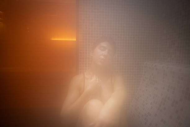 A woman is seen through the hazy mist of a steam room, relaxing and enjoying the detoxifying atmosphere.