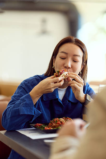 Asian Woman Enjoying A Tasty Bite At A Diner In A Casual Blue Jacket