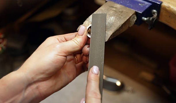 Professional jeweler filing silver ring on workbench.