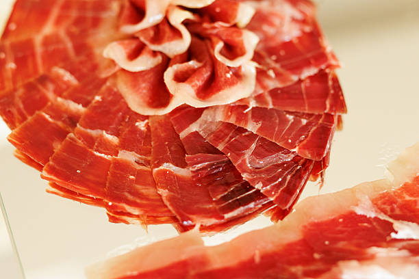 Ham serrano tapas from Spain, Iberian ham from Spanish tapas folded in a row on a dark wood background board.