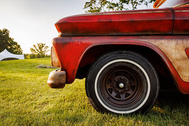 Close-up view of the wheel and fender of a vintage red truck parked outdoors on grass.