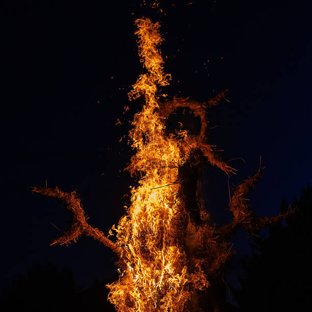 A large straw figure burns intensely against the dark night sky. The photograph emphasizes fire movement, glowing sparks, and dramatic contrast.