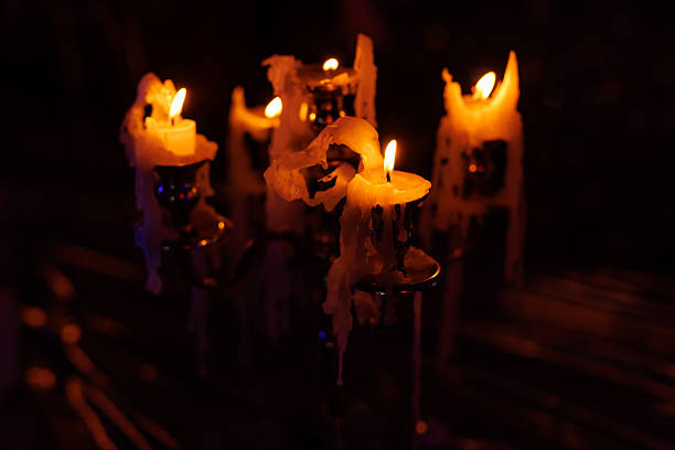 Melting candles burn on an ornate metal candelabra in a dark ambient setting. Warm light, dripping wax and atmospheric decor create a moody scene.