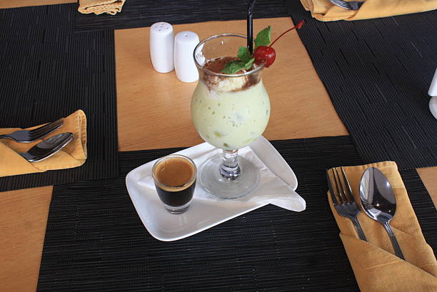 Table setting featuring a creamy green drink with mint and cherry garnish, served alongside a shot of rich espresso Cutlery and salt and pepper shakers complete the dining setup