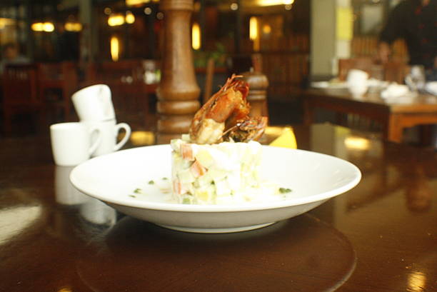 Delicious salad with diced vegetables and creamy dressing, topped with cooked prawns, served on a white plate in an upscale restaurant ambiance