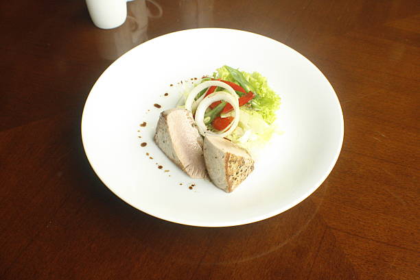 Two pieces of seared fish are served with a fresh mixed green salad, garnished with onion rings, on a white plate atop a wooden table