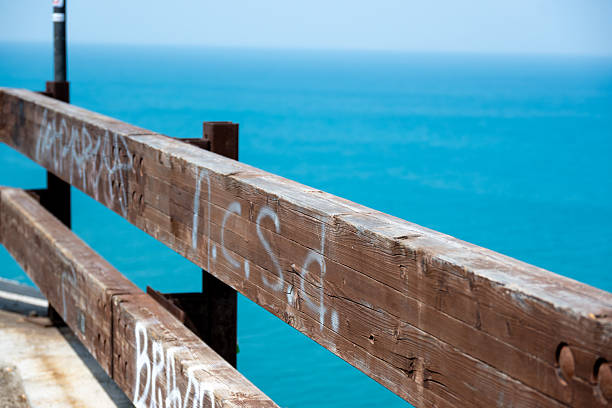 Vieste - Apulia - Italy - 08-29-2025: Close-up of a weathered wooden railing with faded graffiti, with clear turquoise seawater and a distant soft horizon in background.