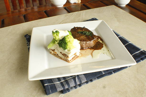 Beautifully plated gourmet steak dinner featuring a perfectly cooked steak topped with a rich sauce, accompanied by a layered broccoli gratin with creamy white sauce