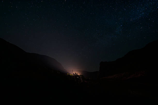 Headlights from a vehicle glow through a remote canyon in Central Oregon, illuminating the surrounding landscape beneath a clear, star-filled night sky.