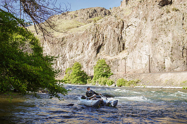 A fly fisherman rows his inflatable raft through a rugged river canyon in Central Oregon.