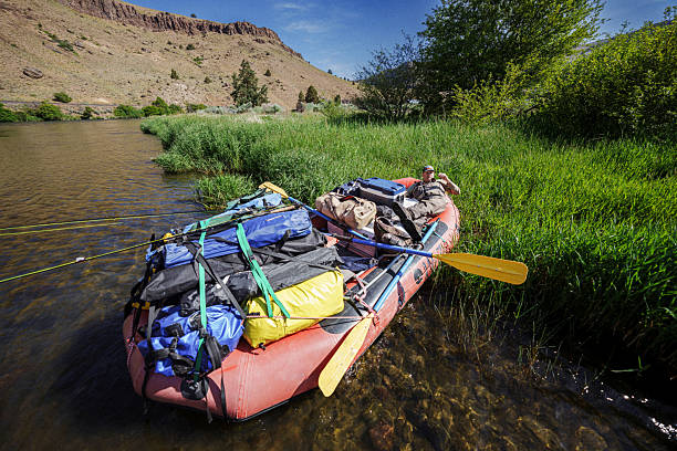 A fly fisherman rests in his gear-loaded raft pulled up along a grassy riverbank along the Deschutes River while on a weekend trip with friends in Central Oregon.