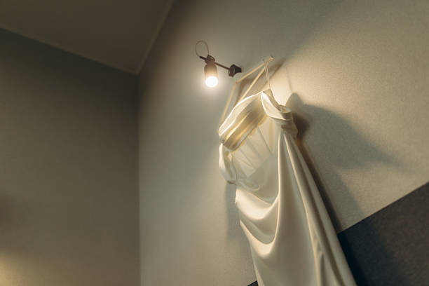 Bridal gown anticipating the ceremony, illuminated by a warm lamp, creating a soft shadow on the wall