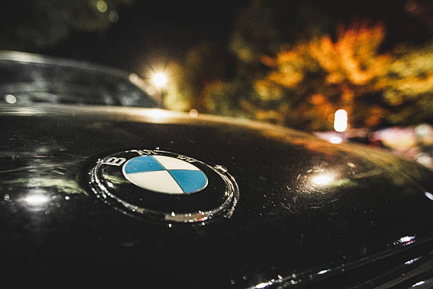 Detailed close-up of the BMW emblem on the hood of a black car with night bokeh lights. Almaty, Kazakhstan - October 04, 2024