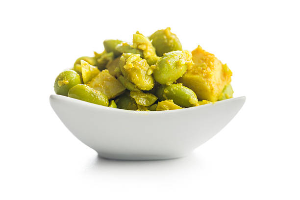 A red serving utensil (spatula, scoop or spoon) emerged in a mixed salad, featuring chunks of red tomatoes, bright green avocado, and pale lima beans.