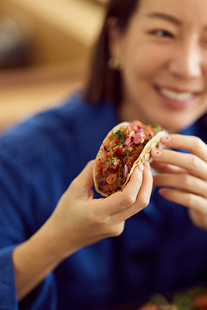 Asian Woman Enjoying A Tasty Taco In A Casual Diner With Bright Lighting And Smiling Expression