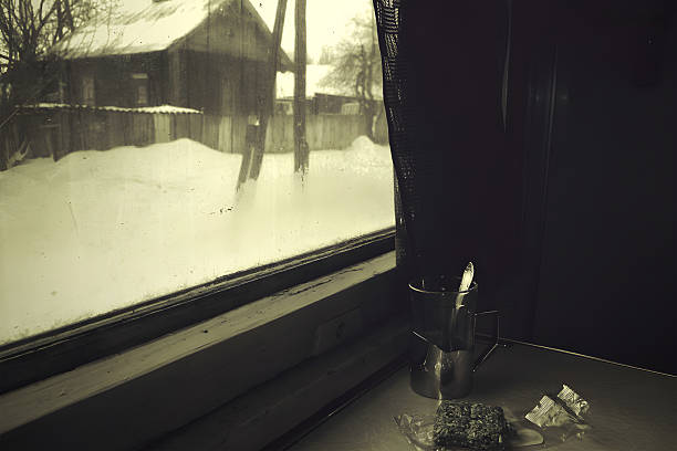 A vintage-toned scene through a frosted train window shows a snow-covered village and a simple metal cup with a spoon on the sill