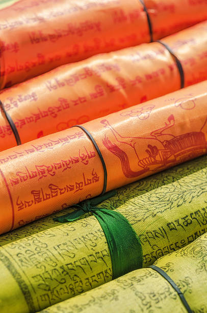 Rolled-up textile scrolls with intricate Tibetan Sanskrit script and illustrations in vibrant orange and yellow colours