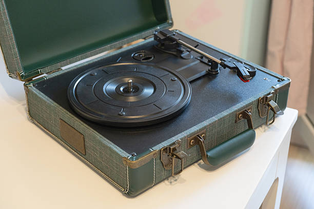 Portable turntable housed in a plaid-covered carrying case with open lid, showing rotating platter and tonearm, designed for analog music playback in modern home setting