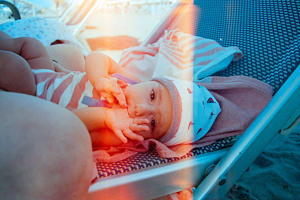 Baby wearing a hat and striped romper relaxing on a beach chair with a towel, enjoying summer vacation. Scanned from analog film