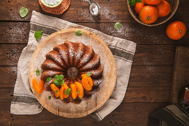 A top-down view of a moist citrus bundt cake garnished with fresh orange segments and mint leaves. Warm, natural side lighting emphasizes the rich texture of the cake and the rustic wood.