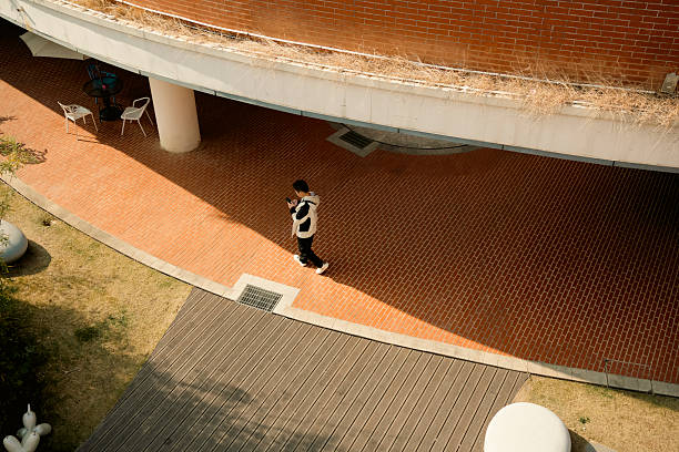 Urban Life in Architecture: A Student Walking Through a Sunlit Courtyard with Curved Red Brick Walls