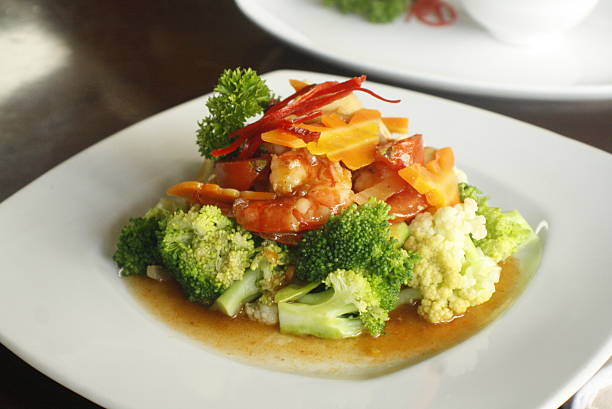Close up of a vibrant stir fried dish featuring savory shrimp, fresh broccoli, cauliflower, carrots, and bell peppers in a rich, flavorful sauce