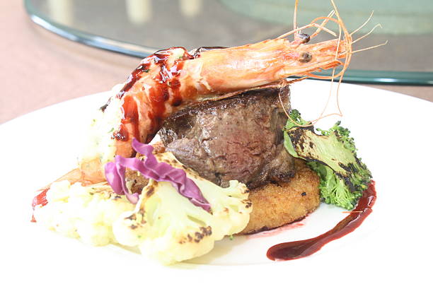 Exquisite gourmet surf and turf dish artfully plated with seared beef steak, a large prawn, grilled vegetables, and a rich sauce, showcasing fine dining