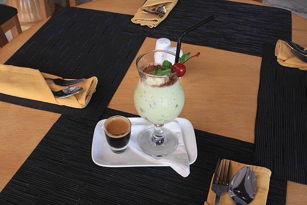 Savor a vibrant green smoothie, garnished with fresh mint and a cherry, accompanied by a strong espresso shot on a white serving tray