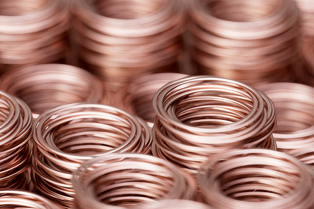 3D rendering of multiple stacks of shiny copper rings or coiled wires. The composition features a repetitive, textured pattern of metallic reddish-brown copper, symbolizing industrial production, electrical engineering, and supply chain logistics. This visual highlights themes of raw material processing, telecommunications infrastructure, hardware manufacturing, and commodity trading. The soft reflections on the metallic surfaces emphasize the high-quality finish of the industrial components.