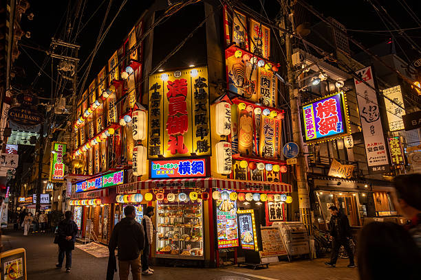 Kyoto, Japan - December 05, 2025: Vibrant night in Osaka's Shinsekai district, showcasing a bustling street with glowing Japanese lanterns, neon signs, and detailed food displays. People enjoy the