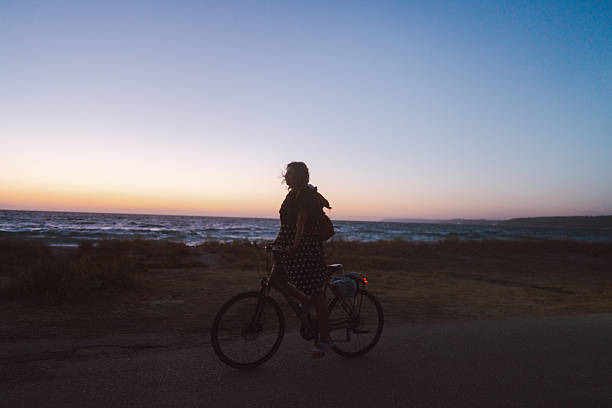 Photo of a cheerful mid adult woman, biking home after day spent on local beach