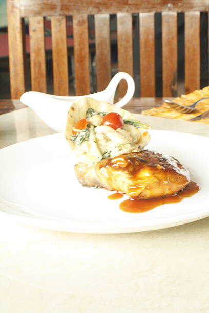 Appetizing meal featuring a piece of glazed chicken or pork alongside a vibrant salad wrap with cherry tomatoes, presented on a white plate in a restaurant setting