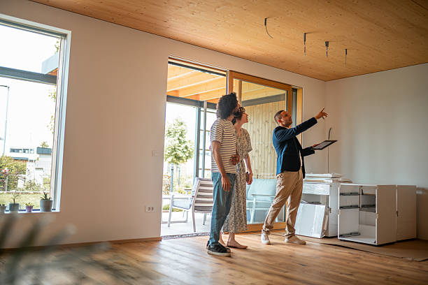 A Hispanic male real estate agent gestures informatively to a diverse couple in a well-lit, spacious home, their interest evident as they envision potential.